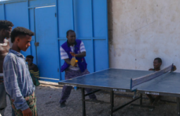 a group of young Ethiopian migrants playing table tennis with IOM staff at IOM's Migration Response Centre in Obock